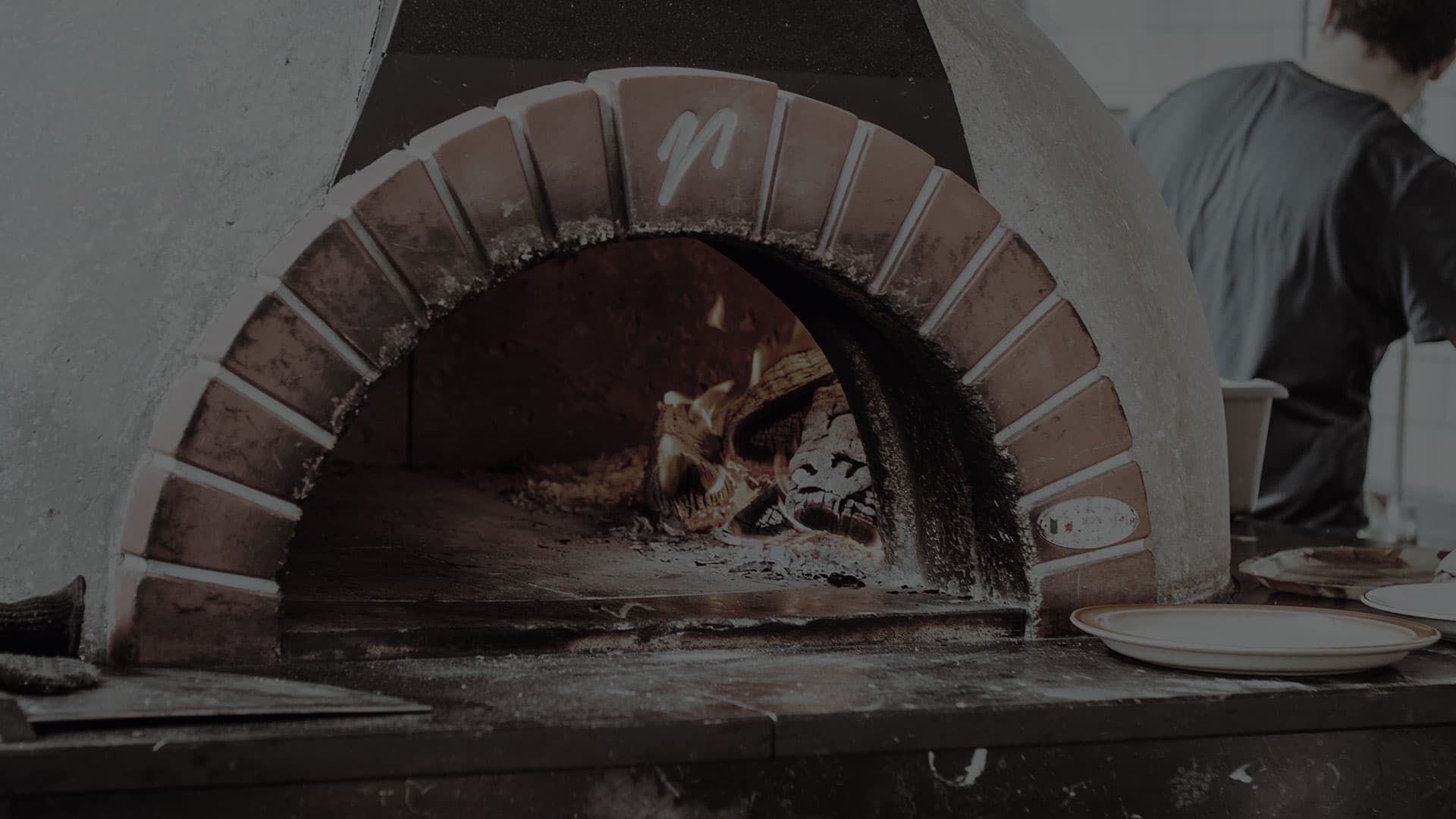 Wood-fired pizza oven with a live fire glowing inside the brick arch